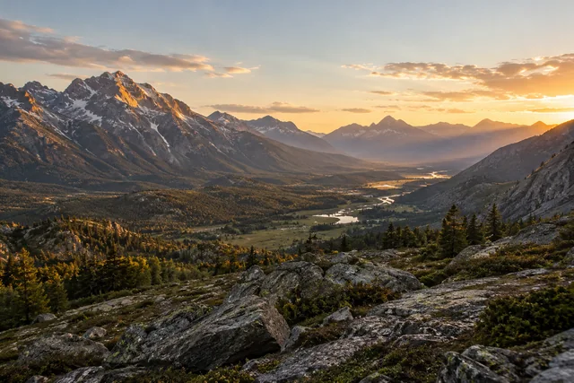 A mountain valley with a bright evening sky and shaded rocky foreground.